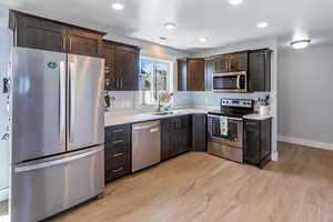 Kitchen featuring light countertops, dark brown cabinetry, appliances with stainless steel finishes, and a sink