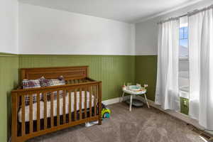 Bedroom featuring visible vents, a wainscoted wall, baseboards, a crib, and carpet floors