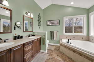 Full bath with vaulted ceiling, a wealth of natural light, a sink, and a garden tub