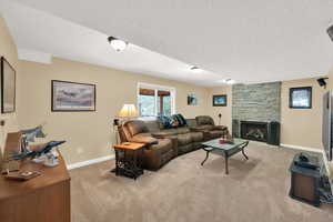 Living room featuring a fireplace, baseboards, light carpet, and a textured ceiling