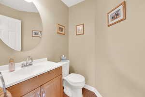 Bathroom featuring vanity, baseboards, wood finished floors, and toilet