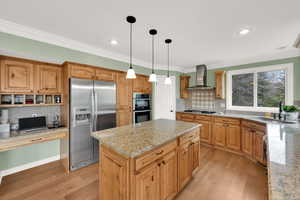 Kitchen with a sink, light wood-style floors, stainless steel appliances, and wall chimney exhaust hood