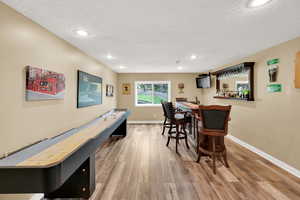 Rec room with bar area, baseboards, a textured ceiling, and wood finished floors