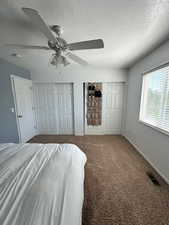 Carpeted bedroom featuring visible vents, multiple closets, baseboards, a textured ceiling, and a ceiling fan