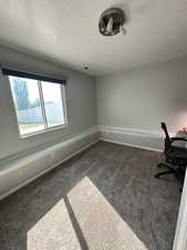Unfurnished office with a textured ceiling, visible vents, baseboards, and dark carpet