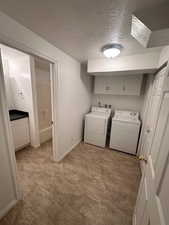 Laundry room featuring a textured ceiling, cabinet space, baseboards, light floors, and separate washer and dryer