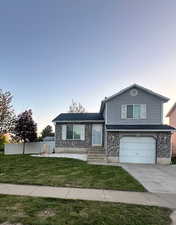 Split level home with an attached garage, fence, a yard, and concrete driveway