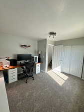 Carpeted home office with baseboards and a textured ceiling
