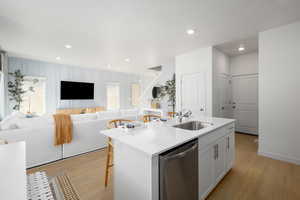 Kitchen with stainless steel dishwasher, open floor plan, a sink, and light wood finished floors