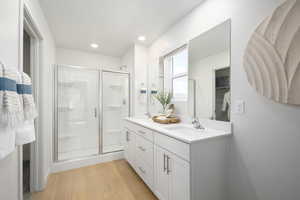 Bathroom with a sink, double vanity, recessed lighting, a shower stall, and wood finished floors