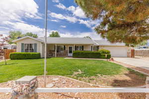 Ranch-style home with a porch, driveway, a garage, fence, and a front lawn
