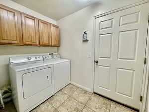 Laundry area featuring baseboards, light tile patterned flooring, cabinet space, and washing machine and clothes dryer