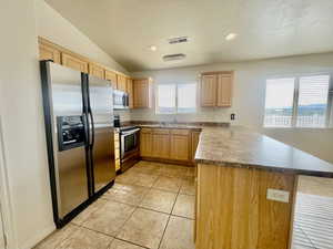Kitchen featuring visible vents, a peninsula, light brown cabinetry, a sink, and stainless steel appliances