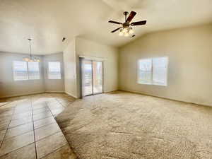 Tiled spare room with visible vents, baseboards, ceiling fan with notable chandelier, and lofted ceiling