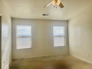 Empty room with a ceiling fan, baseboards, visible vents, and a textured ceiling