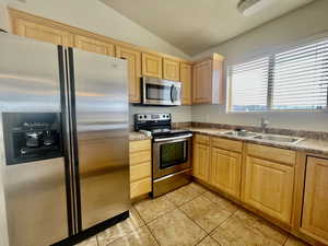 Kitchen featuring light brown cabinetry, vaulted ceiling, a sink, light tile patterned floors, and stainless steel appliances