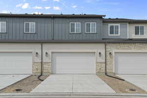 Multi unit property featuring a garage, board and batten siding, driveway, and stone siding