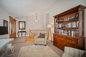 Living area featuring lofted ceiling, light carpet, baseboards, and an upstairs landing