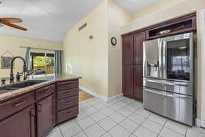 Kitchen featuring visible vents, a ceiling fan, stainless steel refrigerator with ice dispenser, reddish brown cabinets, and a sink