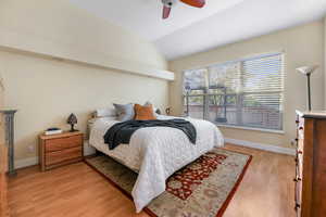 Bedroom featuring a ceiling fan, baseboards, vaulted ceiling, and light wood-style flooring