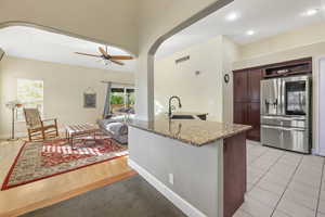 Kitchen featuring light stone countertops, a sink, arched walkways, stainless steel refrigerator with ice dispenser, and visible vents