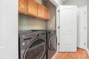 Clothes washing area with light wood-style floors, washing machine and dryer, and cabinet space