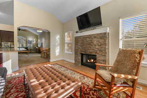 Living room featuring a fireplace, ceiling fan, lofted ceiling, and light wood-style floors
