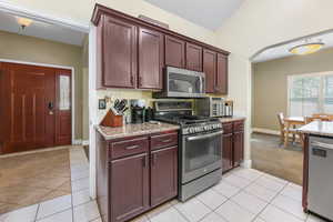 Kitchen with arched walkways, light tile patterned floors, baseboards, light stone counters, and stainless steel appliances