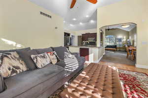 Living area with arched walkways, a ceiling fan, lofted ceiling, light wood-type flooring, and visible vents