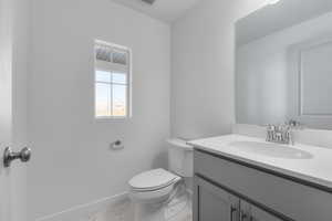 Half bathroom featuring vanity, toilet, marble finish floor, baseboards, and visible vents