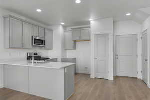 Kitchen featuring light wood-type flooring, gray cabinetry, a peninsula, stainless steel appliances, and recessed lighting