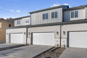 View of property featuring board and batten siding, an attached garage, concrete driveway, and stucco siding