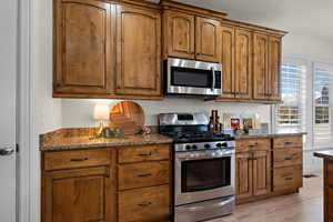 Kitchen featuring dark stone counters, appliances with stainless steel finishes, brown cabinetry, and a textured ceiling