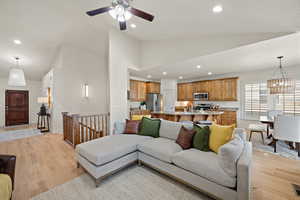 Living area with recessed lighting, high vaulted ceiling, light wood finished floors, and ceiling fan with notable chandelier