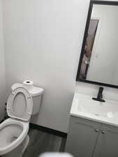 Bathroom featuring vanity, baseboards, wood finished floors, and toilet