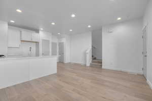 Kitchen with recessed lighting, light wood-type flooring, light countertops, white cabinets, and a sink