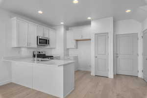 Kitchen with stainless steel appliances, baseboards, white cabinetry, and a peninsula