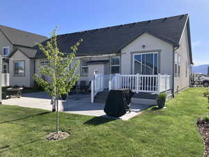 Rear view of property featuring roof with shingles, a wooden deck, a yard, a patio, and stucco siding