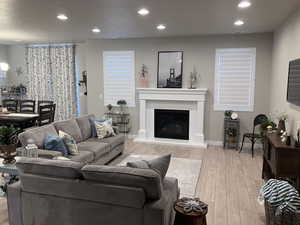 Living room featuring visible vents, light wood-type flooring, baseboards, a glass covered fireplace, and recessed lighting