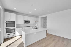 Kitchen with appliances with stainless steel finishes, a sink, white cabinets, light wood-style floors, and recessed lighting