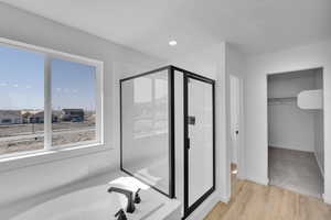 Full bath with a garden tub, a stall shower, wood finished floors, baseboards, and a spacious closet