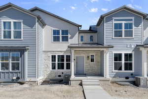 View of front of home with central AC, a standing seam roof, metal roof, and stone siding