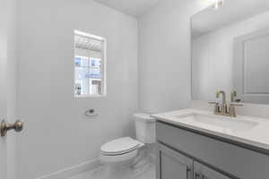 Bathroom featuring baseboards, marble finish floor, toilet, and vanity