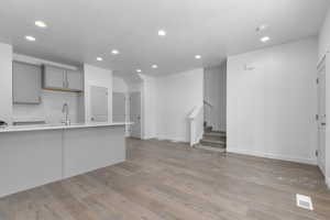 Unfurnished living room featuring visible vents, stairs, a sink, light wood-style floors, and recessed lighting