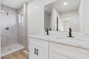 Full bathroom with a sink, double vanity, a tile shower, and wood finished floors