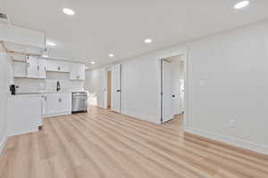 Kitchen featuring open shelves, stainless steel dishwasher, a sink, light wood finished floors, and white cabinetry