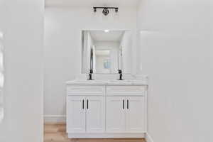 Bathroom featuring a sink, baseboards, double vanity, and wood finished floors