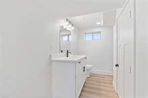 Half bath with visible vents, vanity, wood finished floors, toilet, and baseboards