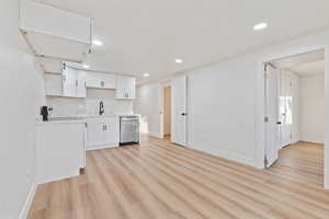 Kitchen with white cabinets, a sink, dishwasher, light countertops, and light wood-type flooring