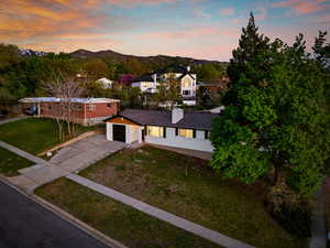 View of front of property with an attached garage, aphalt driveway, a mountain view, a chimney, and a lawn